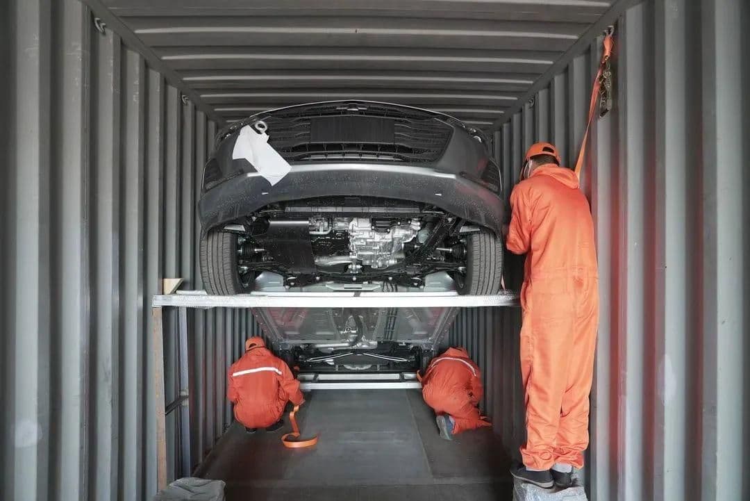 Workers lashing a car onto a loading frame inside a shipping container